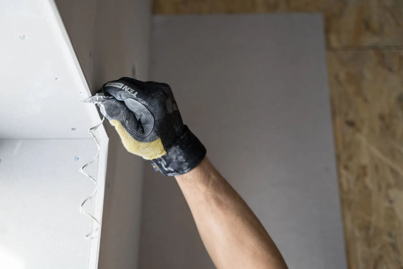 Gloved hand scraping loose material from a damaged wall before patching and painting
